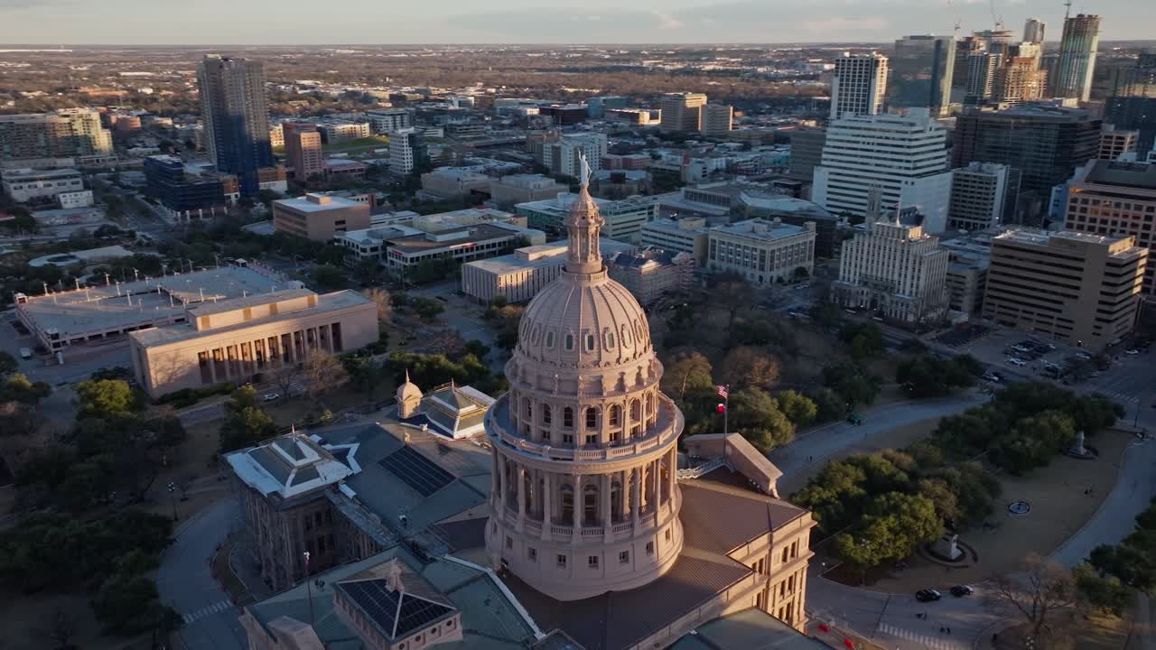 A drone shot circling the Texas State Capitol building in Austin Texas at sunset facing away from the sun with the sun illuminating the Goddess of Liberty statue on top of the dome