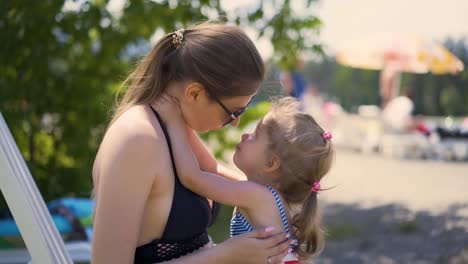 madre e hija de primer plano están sentadas en la playa cerca de arbustos con gafas de sol