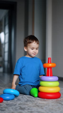 beautiful caucasian baby sits on the floor constructing the pyramid. toddler learns colors, shapes and sizes through the game. vertical video.