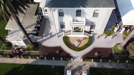 aerial top down panning over a white villa with palms and flowerbeds around