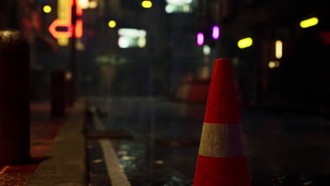 a lone traffic cone stands on a wet city street at night.