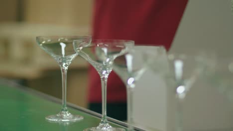 rows of glassware on conveyor belt ready for packaging by worker in background at glass factory