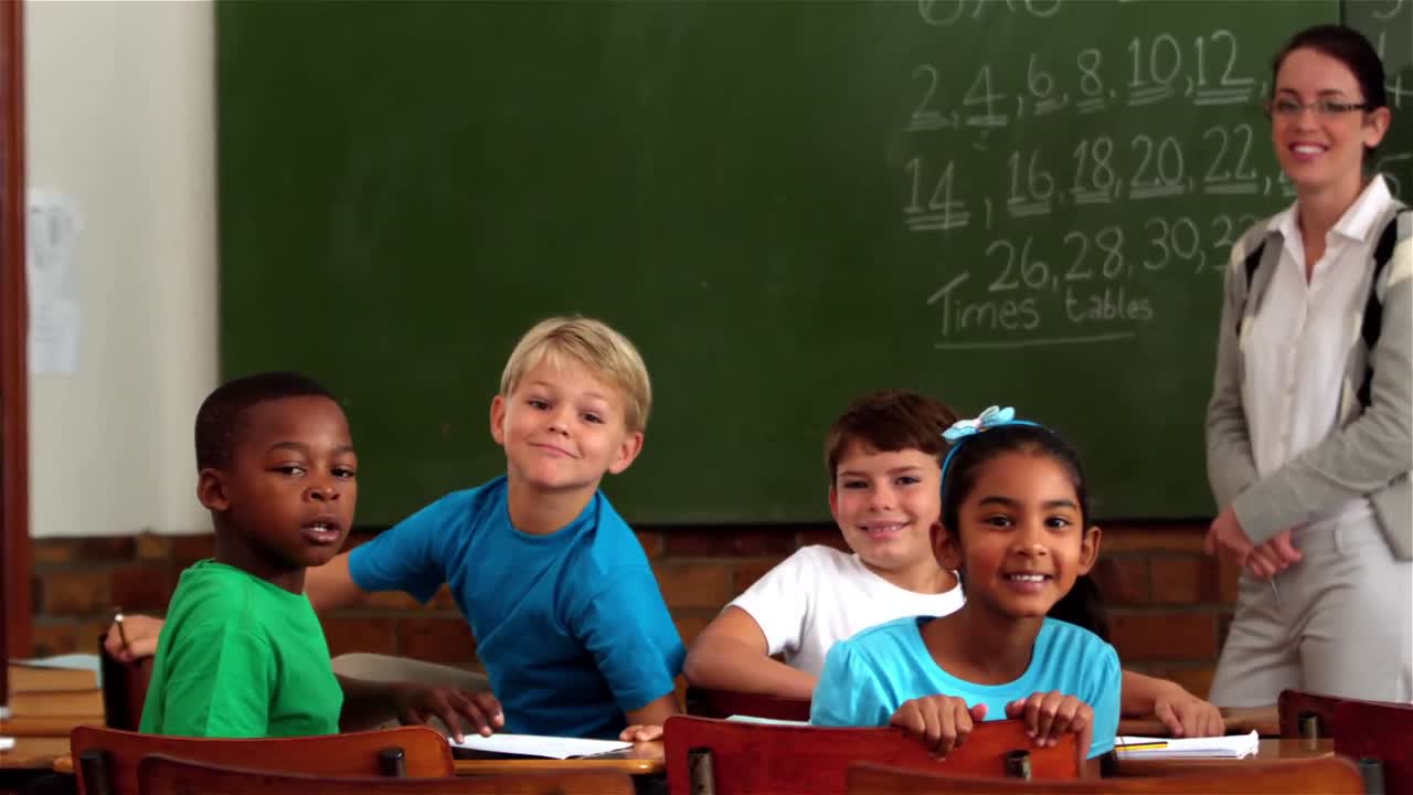 Teacher and young pupils smiling at camera in classroom