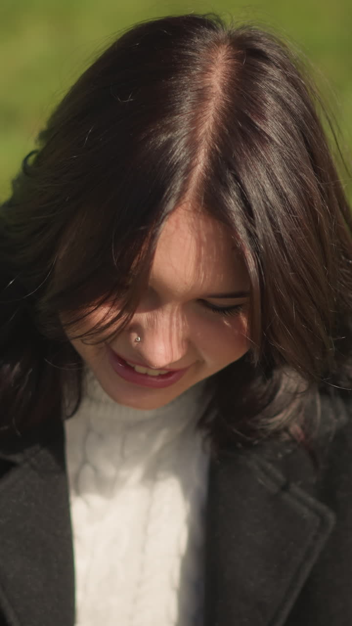 바람이 부드럽게 그녀의 머리카락을 날려, 배경에 무언가에 초점을 맞추고, 평화로운 야외 환경에서 초록색으로 둘러싸인 기쁜 여성