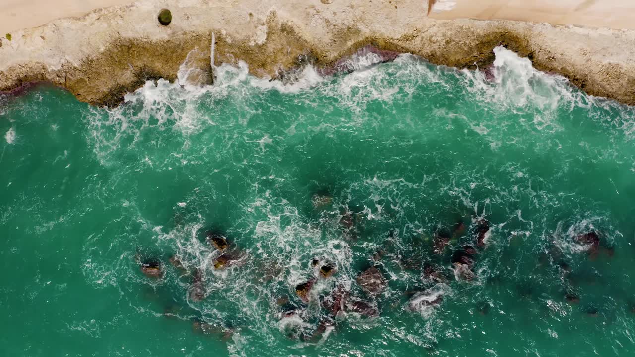 top down drone aéreo disparado de olas que se estrellan contra las rocas de la costa en un soleado día de verano. costa con acantilados. agua del mar mediterráneo desde arriba.