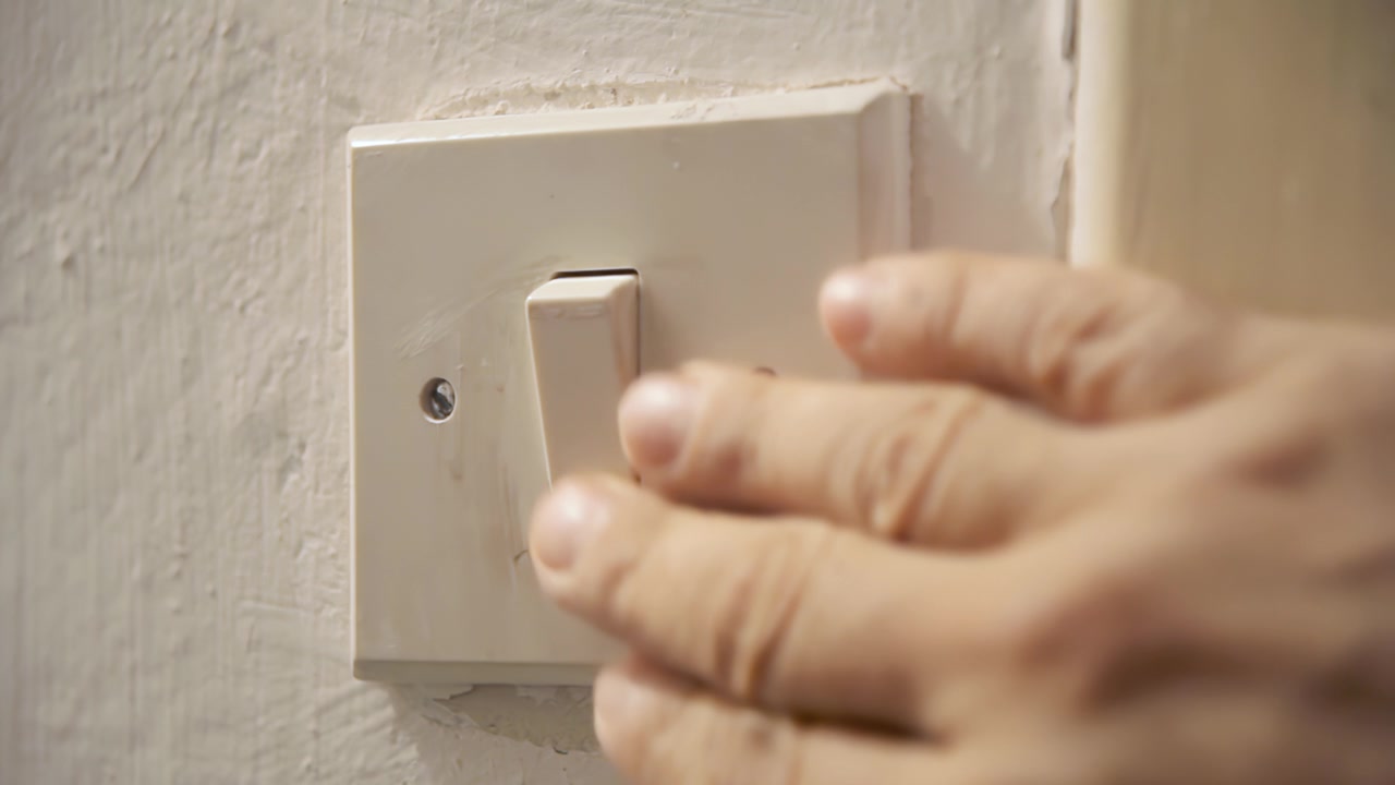 A scared cautious hand seeks in the dark for an old worn light switch, turning it on and off