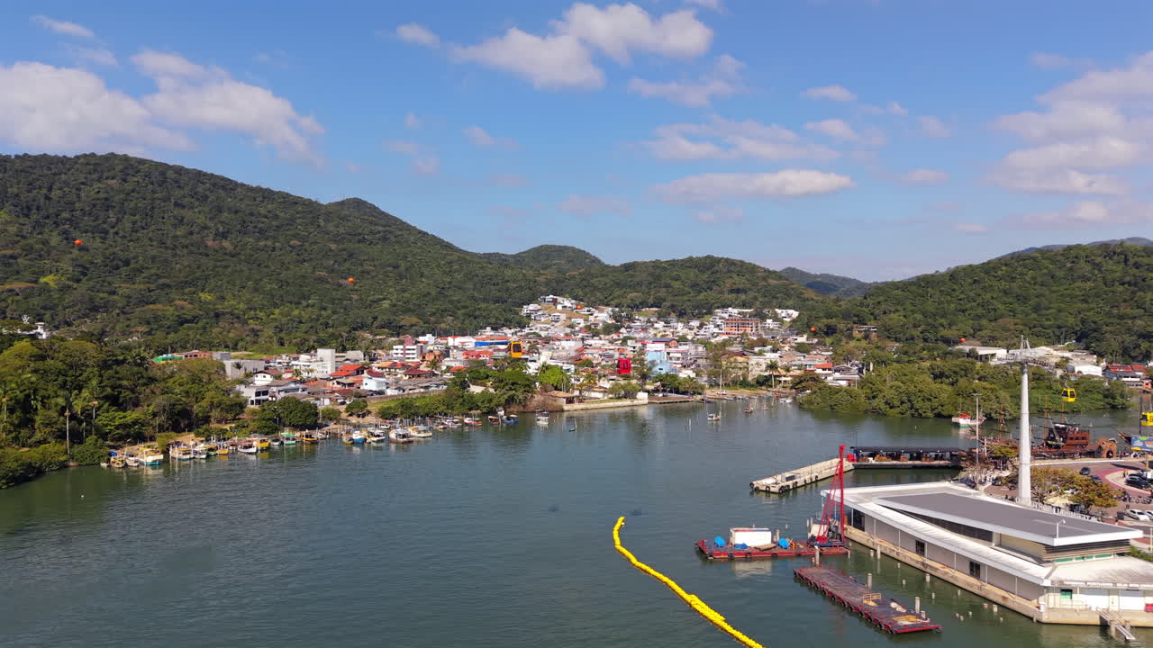 A stunning aerial view of Balneário Camboriú's coastline, featuring the bustling harbor, vibrant town, lush green mountains, and cable cars traversing the sky