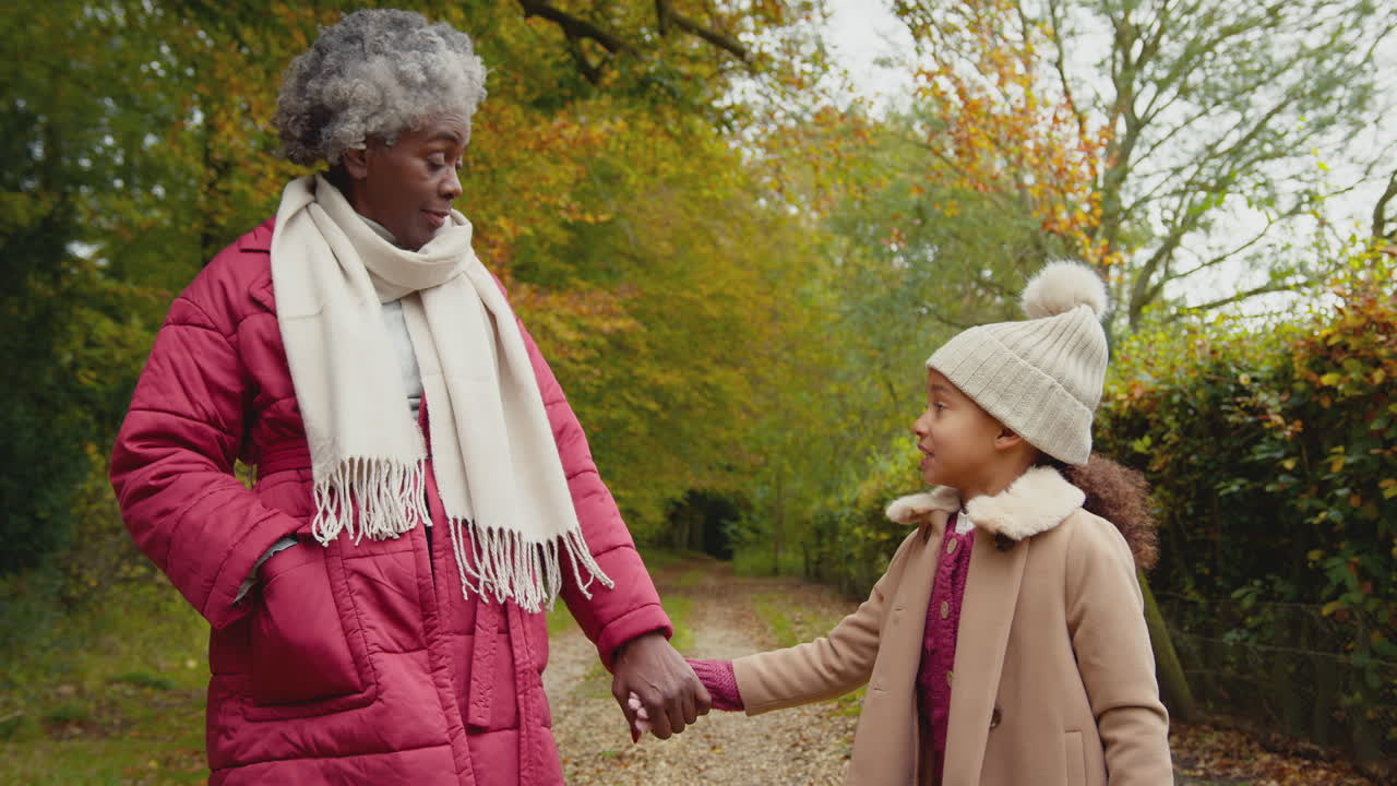 Nonna sorridente che tiene per mano la nipote mentre camminano insieme nella campagna autunnale - ripreso al rallentatore