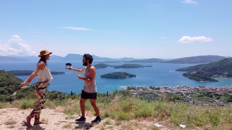 a young couple poses at a viewpoint above the town of nidri, greece