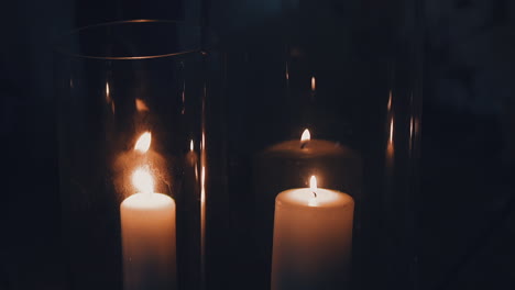 burning white candles in glass holders on black background