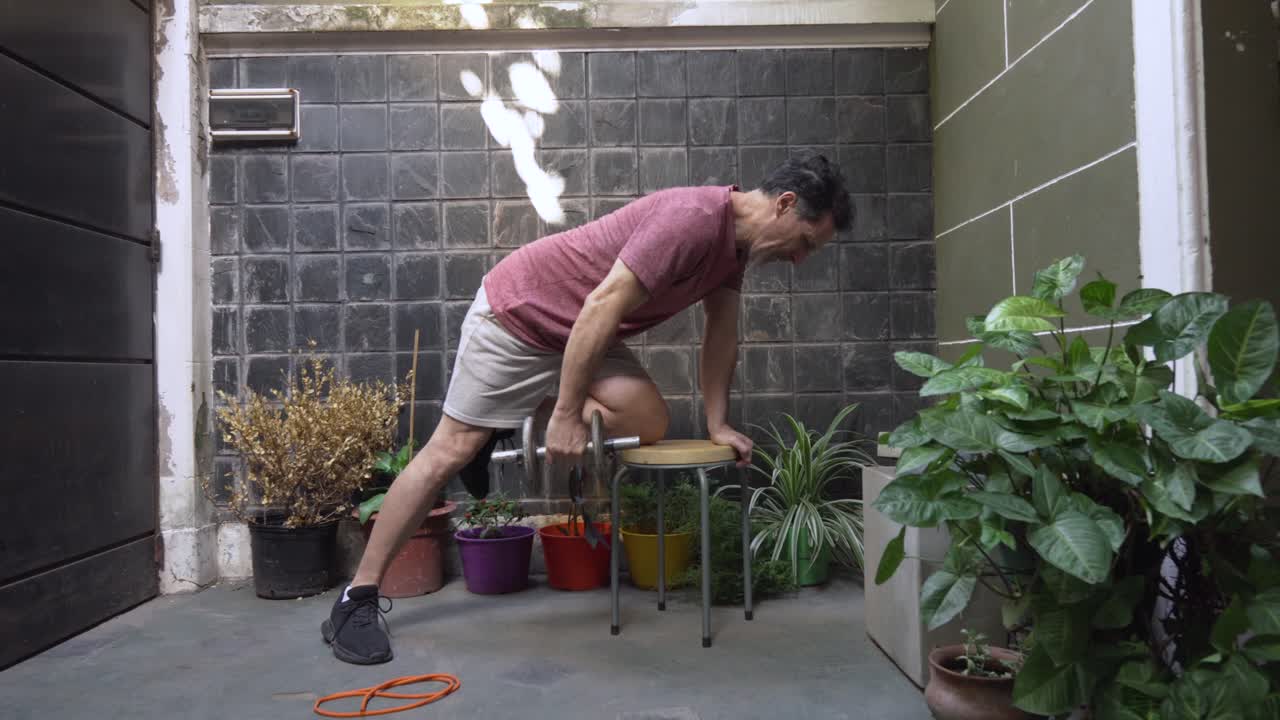 Active mature man uses a stool for stability to perform a bent-over dumbbell row, targeting his lats and upper back as part of his fitness routine