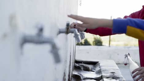 tres personas se acercan a los grifos naturales para llenar botellas de agua