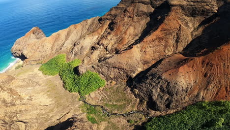 Vista-Aérea-De-La-Costa-Azul-Y-Las-Olas-Rompiendo-A-Lo-Largo-De-Las-Colinas-Ondulantes-En-Kauai-Hawaii