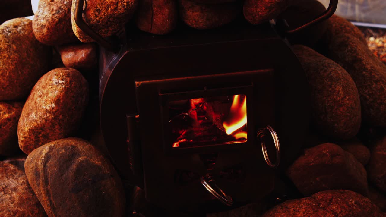 뜨거운 바위로 둘러싸인 아늑한 나무 난로에서 주황색 불꽃이 타오른다