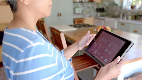 focused senior biracial woman using tablet with smart home on screen at home