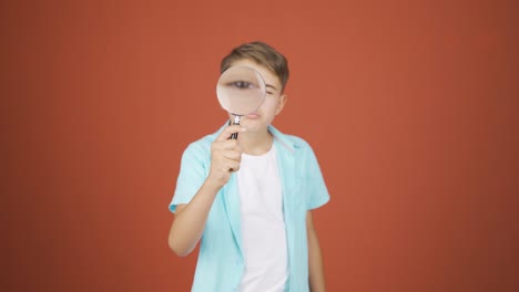 boy looking at camera with magnifying glass.