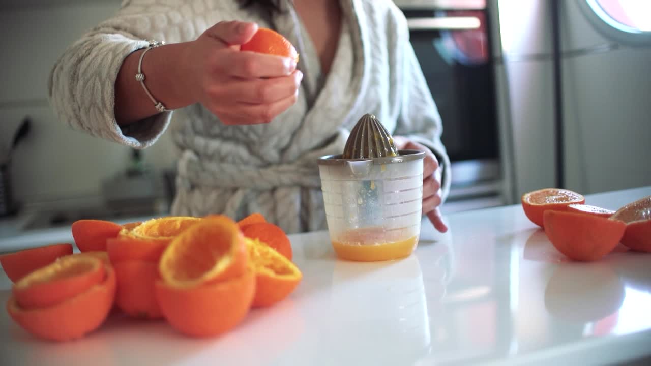 Mujer usando un exprimidor de naranjas, preparando un zumo de naranja en casa.