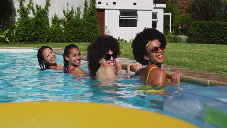 diverse group of female friends standing at the poolside looking at the camera
