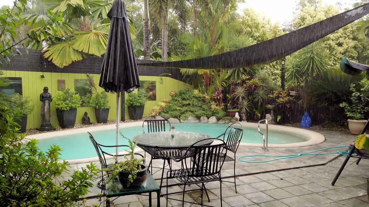 A beautiful outdoor pool surrounded by lush, green plant life in Queensland, Australia on a heavy rainy day - Wide Shot