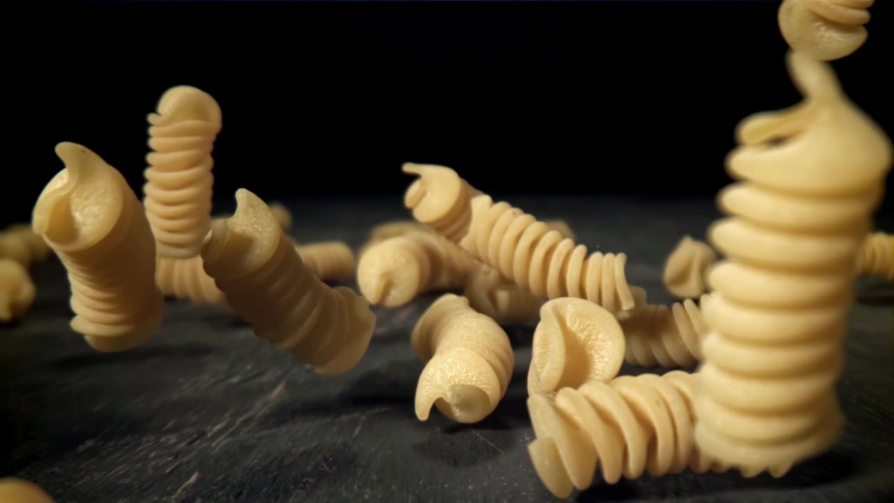 Fusilli secchi che cadono su una superficie scura al rallentatore