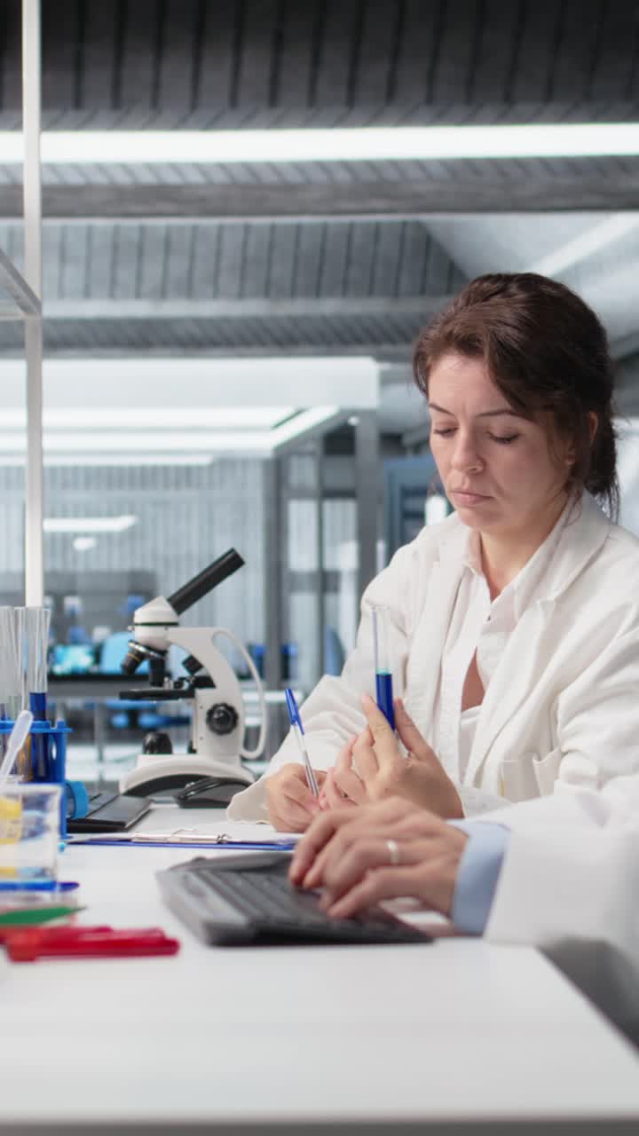 Vertical video Chemist using laboratory glassware with indicator solution next to coworker