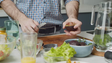 primer plano de las manos del hombre quitando un hoyo de un aguacate con un cuchillo en una cocina de estilo moderno