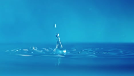 vídeo en 4k en cámara lenta de una superficie de agua con gotas que caen sobre un fondo azul. salpicaduras de agua. rodaje de estudio.