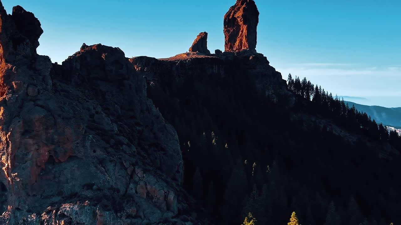 Gün ışığında uzun ağaçlar ve kayalık oluşumlarla Gran Canaria manzaraları.