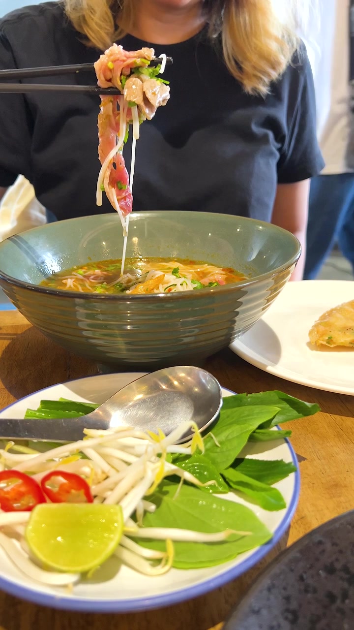 Một người thưởng thức phở Việt Nam với nguyên liệu tươi ngon trong không gian nhà hàng ấm cúng, làm nổi bật sự thưởng thức ẩm thực và sự giao thoa văn hóa.