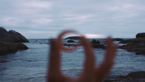 close-up-of-hand-holding-seashell-on-cloudy-seaside-beach