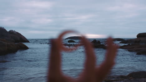 cerca de la mano sosteniendo una concha de mar en una playa costera nublada