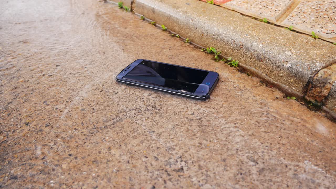 Waterproof modern smartphone lying in the street getting wet from rain runoff
