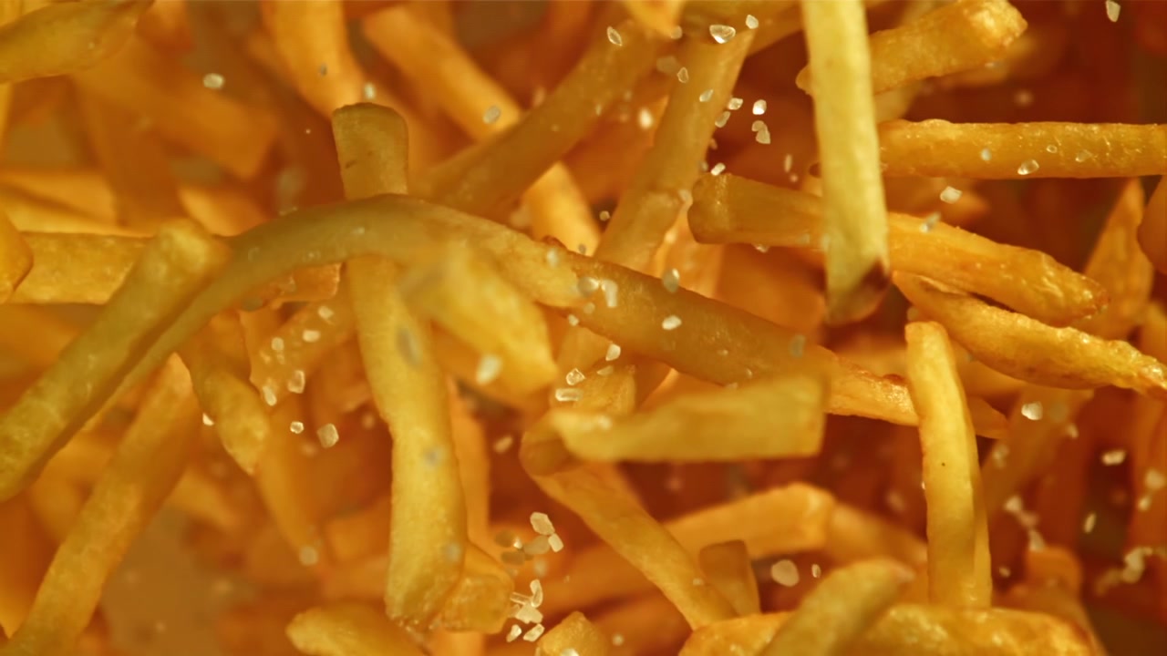 Närbild på salt som faller på gyllene pommes frites i slow motion