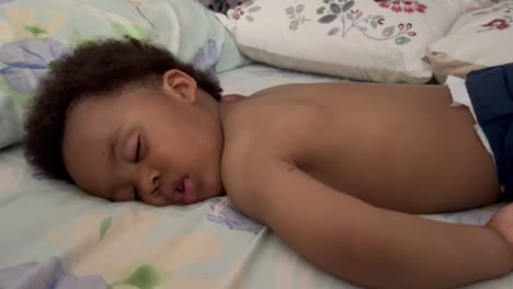 exotic and cute two year old afro european child sleeping a summer siesta in his bed