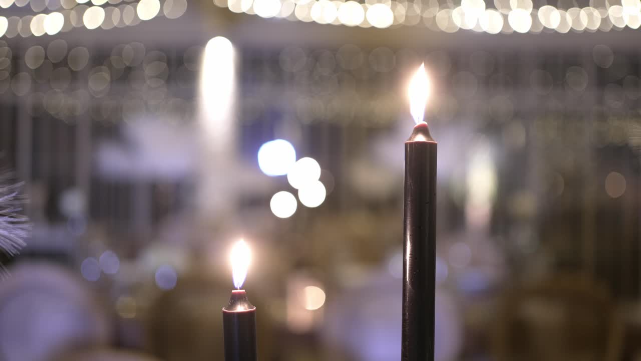 two lit candles glow with warm bokeh lights in soft focus festive evening setting