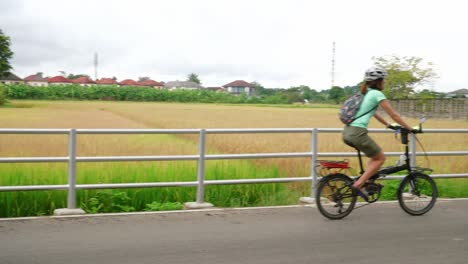 asian female slowly riding bike on paved road in rural town during day, thailand