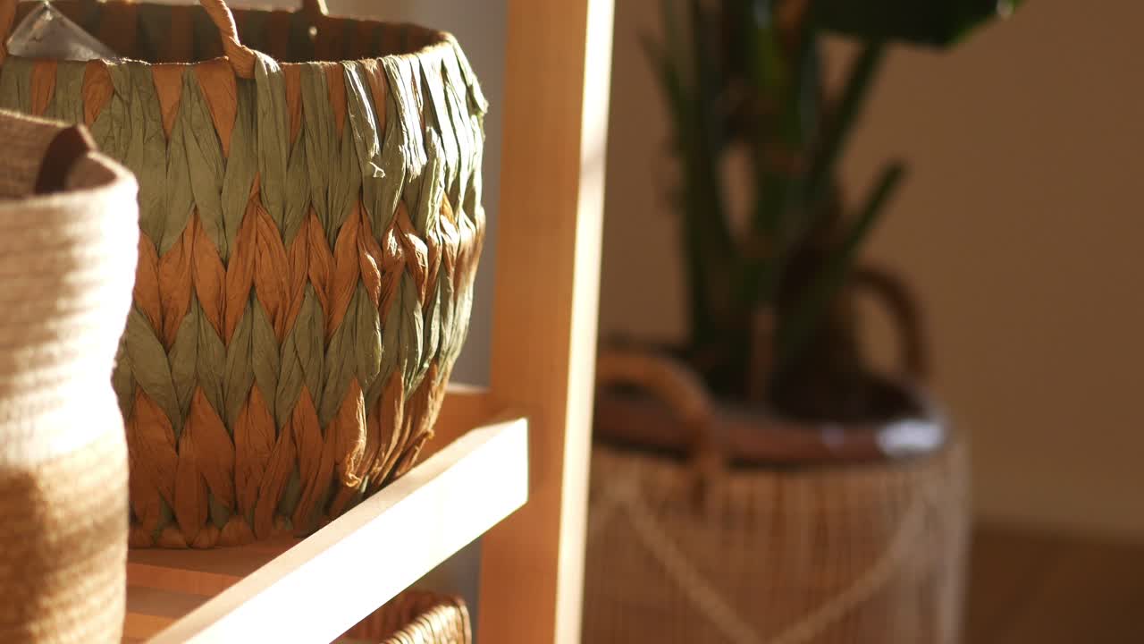 Close-up of a decorative woven basket on a shelf with a blurred plant in the background