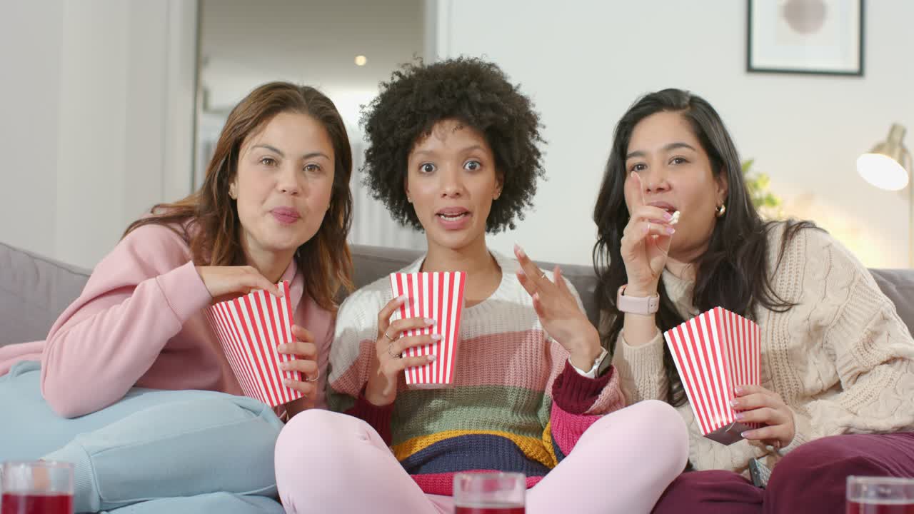 Tre väninnor i soffan viskar, reagerar på spänningen, tar popcornhinkar och skrattar.