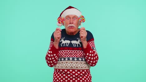 grandfather in christmas sweater holding candy striped lollipops hiding behind them, fooling around