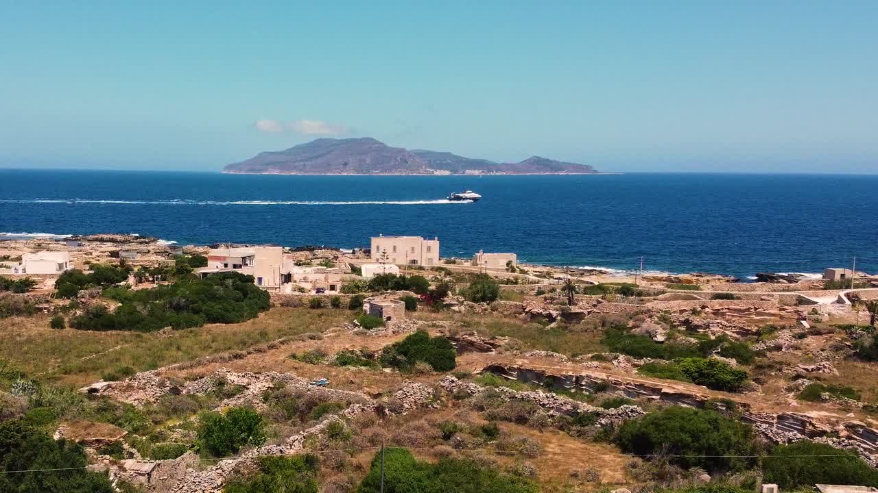 Luftfoto af Favignana-øen, Egadi-øerne, Sicilien. Gamle stenruiner i forgrunden, dybblåt Middelhav og Levanzo-øen i horisonten. En speedbåd krydser billedet