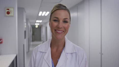 portrait of caucasian female doctor standing in corridor laughing looking at camera