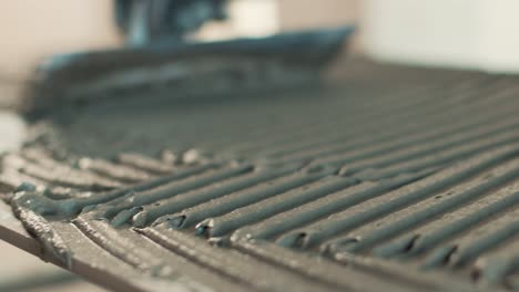 using a notched trowel to spread tile adhesive on a floor