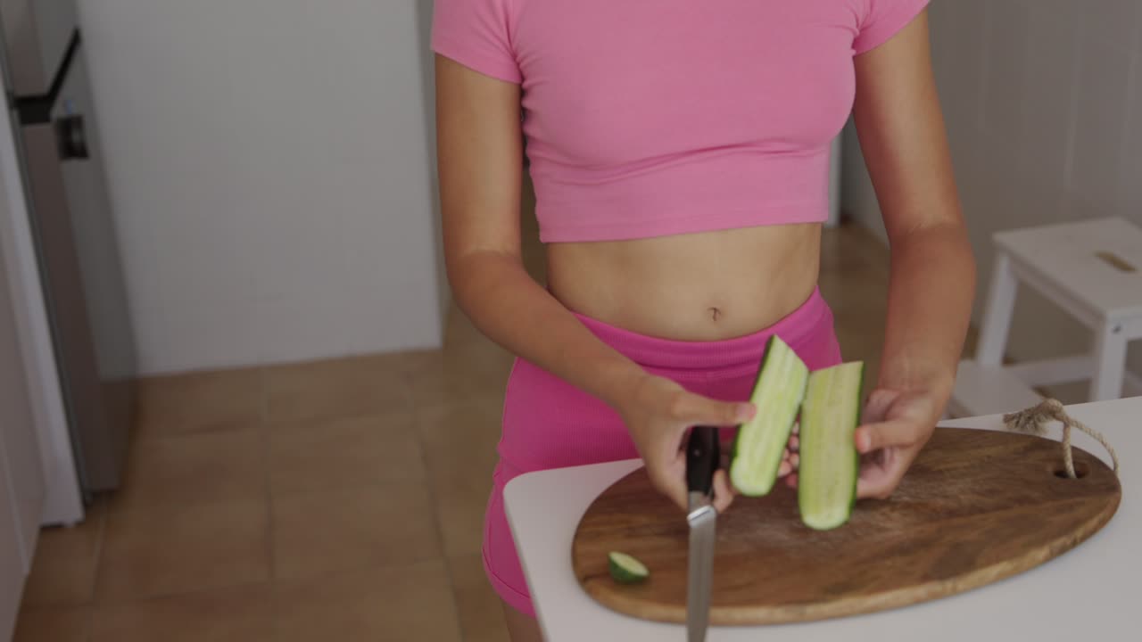 Woman cutting cucumber in kitchen