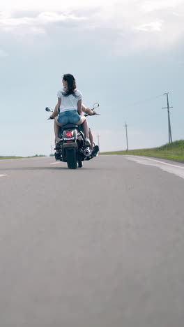 low angle shot young man and woman ride black motorcycle along country asphalt road under summer cloudy sky