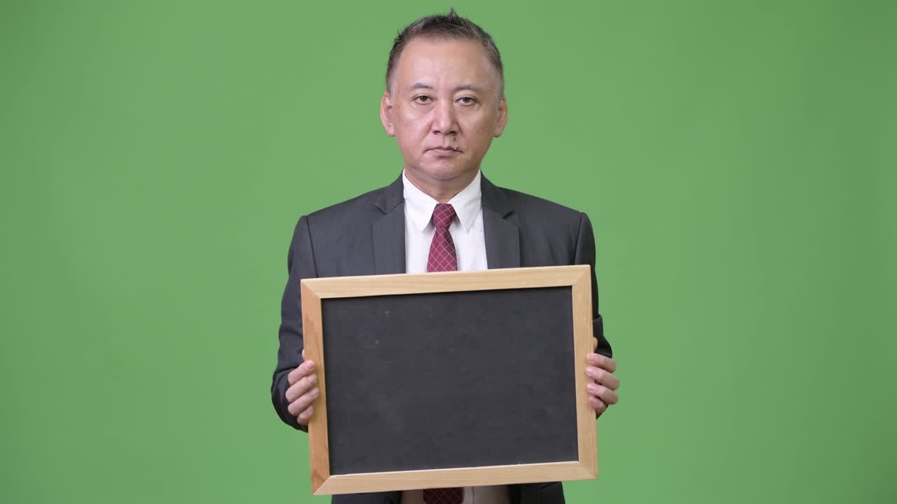 성숙 한 일본인 사업가 가 초록색 배경 에 검은판 을 들고 있다