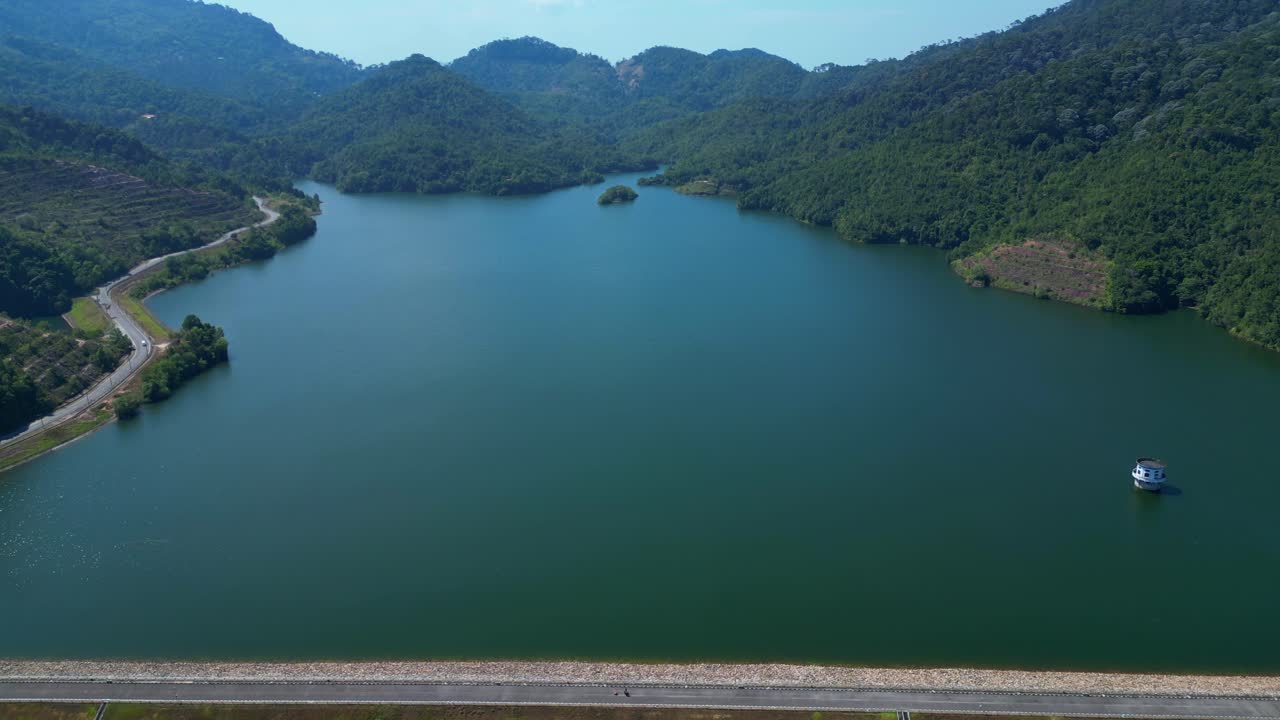 Luftfoto af en stor dæmning og et reservoir i et bjergrigt landskab.