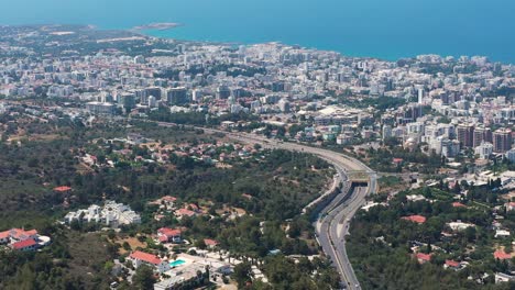 Volando-Por-Encima-De-Una-Autopista-Con-Vistas-A-La-Ciudad-En-Expansión-Hacia-El-Mediterráneo