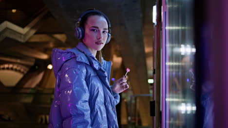 Girl-touching-snack-automat-making-choice-standing-in-night-city-subway-close-up