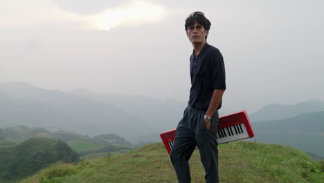 handsome elegant asian man walking on hilltop holding an electronic piano