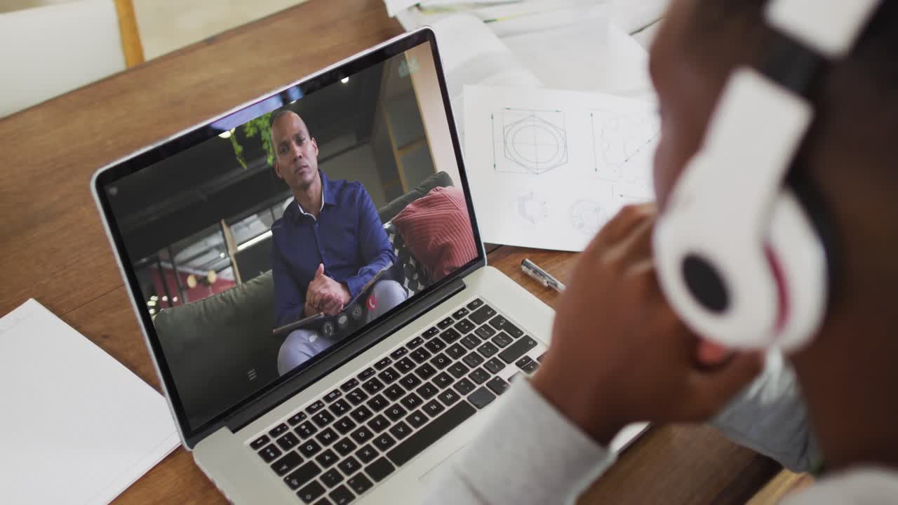 African american businessman sitting at desk using laptop having video call with male colleague